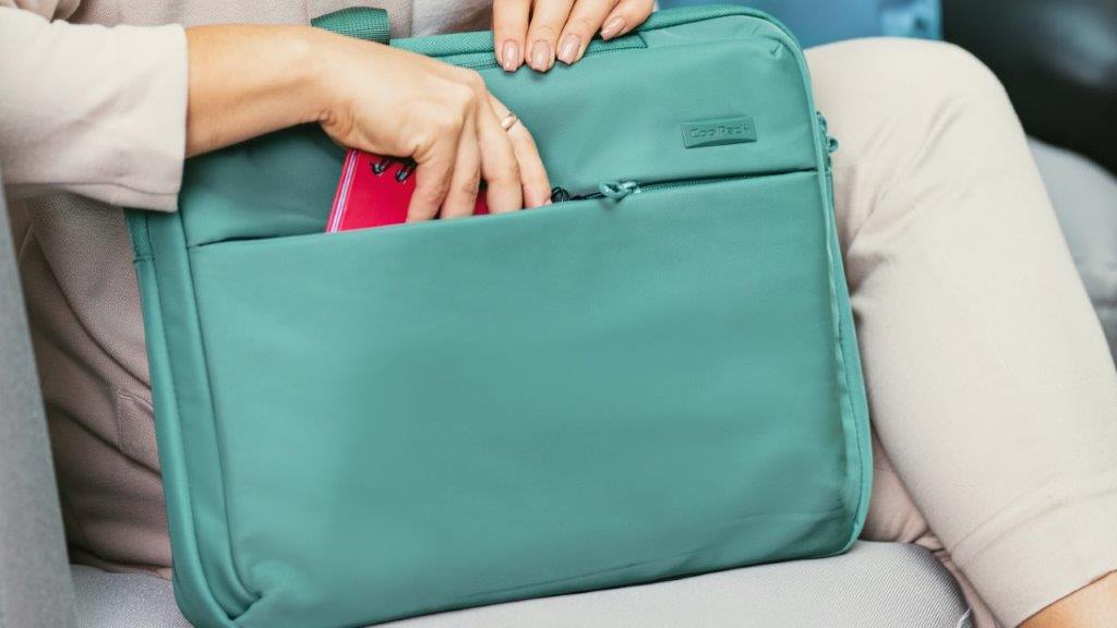 Moteris deda daiktą į žalią CoolPack kompiuterio rankinę